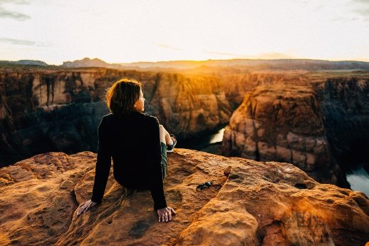 Mindset ändern - Frau sitzt auf einer Klippe beim Sonnenaufgang